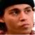 A pixelated close-up of a person's face with a dark cap, visible eye, nose, mouth, and partial ear, set against a dark background.