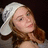 A pixelated image of a person with light brown hair wearing a white towel on their head, set against a dark background.