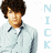 A pixelated image of a person with curly brown hair wearing a light blue jacket over a white shirt, with vertical text reading "NICK" in light blue letters to the right.