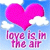 A pixelated image shows a large pink heart floating above white clouds against a light blue sky, with the text "love is in the air" in pink lettering below.