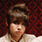Pixelated image of a person with dark hair styled upward, wearing a light-colored top against a red patterned background.