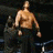 A shirtless man in black pants appears in four sequential poses: standing, being lifted by another figure, shouting into a microphone, and raising arms upward.