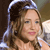A pixelated close-up of a person with light brown hair wearing a blue headband, holding a microphone near their mouth.