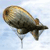 Pixelated fish-shaped icon with brown and gray tones, dark eye, and a small tail fin, set against a light blue background.