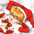 Pixelated character with blonde hair and blue eyes wears red Santa hat and red-and-white outfit, holding red object, against light background.