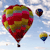 A static image of three hot air balloons floating against a light blue sky with scattered white clouds, the largest balloon in the foreground displaying a mix of red, green, and yellow patterns.