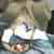 Pixelated static image of a figure with light hair and dark clothing against a blurred background, showing partial facial features and indistinct surroundings.