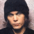 Pixelated portrait of a person with dark hair and light skin wearing a black top against a muted background.