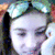 Pixelated static image of a person's face with closed eyes, wearing a dark headband and light-colored clothing against a blurred background.