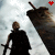 Silhouette of a figure holding a sword stands before a large weapon against a cloudy sky, with red and black heart symbols above.