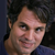 Pixelated close-up of a person's face with dark hair and light skin, wearing a blue garment against a dark background.