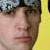 A static close-up of a person's face with a yellow background, wearing a dark cap with a light patterned section.