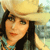 Pixelated image of a person wearing a light brown cowboy hat, dark hair, and a turquoise top with dark patterns.