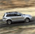 Pixelated silver SUV with dark windows and black wheels on a blurred background of horizontal brown and beige stripes.