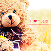A pixelated brown teddy bear with white earbuds wears a dark blue shirt with white trim, holding a yellow flower, next to red text reading "I ❤️ MUSIC" on a blurred yellow-green background.