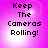 Four identical display 'Keep The Cameras Rolling!' text on a pink gradient background with pixelated text and light effects