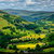 Pixelated landscape with layered green and yellow fields under a blue sky with light clouds.