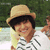A person wearing a straw hat and striped shirt smiles in a pixelated image with green foliage background.