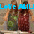 Two women in long dresses stand side-by-side with arms raised, one in green floral dress, the other in red patterned dress, under blue text reading "Love AIME!".
