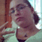 Pixelated image of a person with short brown hair and glasses, wearing a light-colored top against a blurred background.
