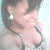 A woman with dark hair and earrings wears a patterned top, her head slightly tilted in a static pose.