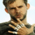 Static pixelated image of a man's face and upper torso with short dark hair, light skin tone, visible beard stubble, wearing a dark jacket over a white shirt with a patterned tie or collar detail.