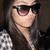 A pixelated close-up of a person with long dark hair wearing sunglasses and a light-colored top, cropped to show only the upper body.
