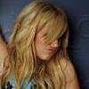 A static image of a person with long wavy blonde hair lying on a dark blue surface, wearing a light-colored top with dark patterns.