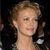 Pixelated close-up of a person with light brown hair styled in an updo, wearing a dark garment with a white circular detail on the shoulder.