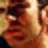 Pixelated close-up of a person's face with warm brown and orange tones, showing partial facial features including eyes, nose, and mouth.