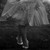A grayscale pixelated image of a figure with a long neck and rounded head, standing against a dark background with light areas above.