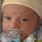 A baby wearing a light yellow beanie and white shirt with blue accents, shown in four with slight facial expression changes