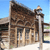 Pixelated image of a brown wooden structure with vertical posts and a sloped roof under a blue sky.