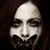 Pixelated static image of a stylized face with closed eyes, dark eyebrows, and a wide mouth showing teeth, set against a dark background.