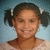 Pixelated portrait of a person with dark hair in two pigtails, light skin tone, smiling expression against blue background.