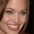 Pixelated close-up of a smiling person with light brown hair, visible teeth, and brown eyes against a dark background.
