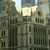 Pixelated image of a multi-story stone building with arched windows and decorative stonework under a light sky.