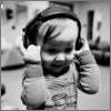 Black-and-white photo of a child wearing headphones, holding them with both hands, in a blurred indoor background.