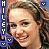 Pixelated static image of a person with light brown hair and a smiling expression, featuring vertical text on the left side.