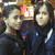 Two people in dark clothing with white stripes pose closely together in a group photo with a blurred background.
