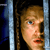 Static pixelated image of a person's face partially visible between vertical bars, with dark hair and light skin tones against a black background.
