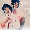 Two figures in white shirts and dark hats pose against a light background with red accents on clothing.