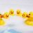 Yellow rubber ducks float in a white tub with blue water, surrounded by red pixelated text on a blue background.