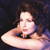 Static pixelated image of a person with long brown hair resting their chin on one hand, wearing a dark top against a dark background with purple and blue tones.