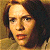 Pixelated close-up of a person's face with light skin, dark hair, and a neutral expression against a warm-toned background.