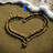 A heart drawn in sand with blue text appearing sequentially: 'I', then 'love', then 'you' over the same background.