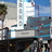 Pixelated static image of a modern building with a tall white tower, blue sky, and palm tree on left, viewed from a low angle.