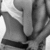Black-and-white image of a person in a white top and dark belt, viewed from behind with hands clasped at the waist.