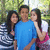 Three people pose outdoors in a group photo with green foliage background; the rightmost person wears pink and white clothing.