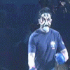 A person in a dark blue shirt with white and red accents performs various poses on stage, wearing blue gloves and pink wristbands under stage lighting.